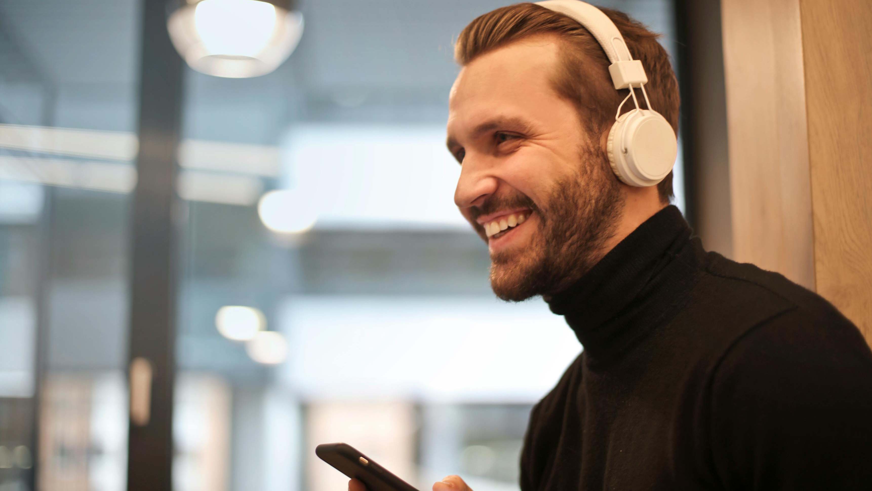 Mann mit weißen kabellosen Kopfhörern und Android-Handy, lächelnd – Anleitung zum Verbinden von Bluetooth-Kopfhörern.