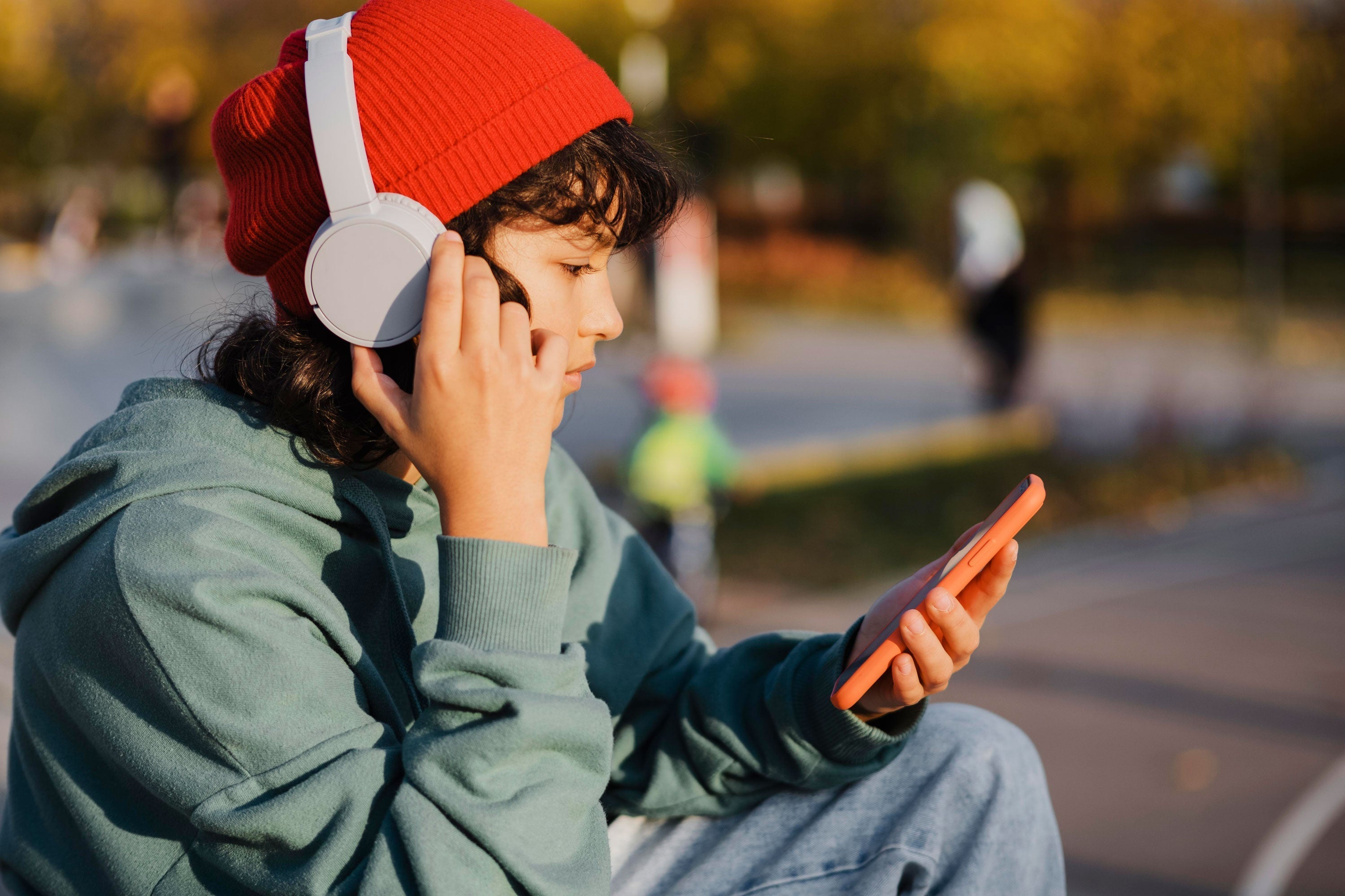 Junge mit roten Mütze und weißen Bluetooth-Kopfhörern nutzt Smartphone im Freien – Update für bessere Leistung.