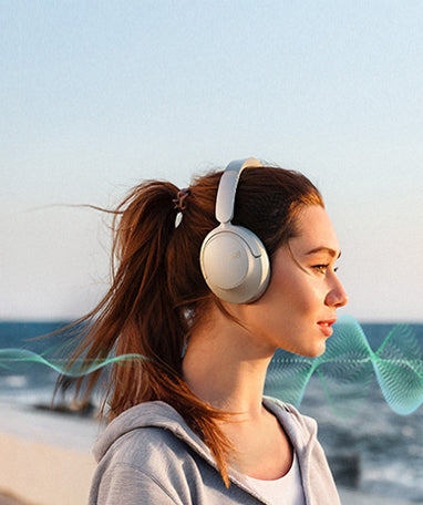 Femme avec des écouteurs blancs Over-Ear à la plage, le vent souffle dans ses cheveux.