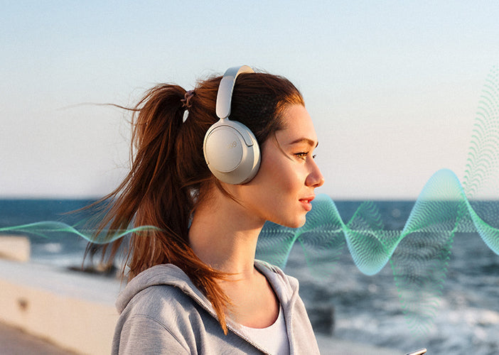 Femme avec des écouteurs sans fil au bord de la mer, écoutant de la musique
