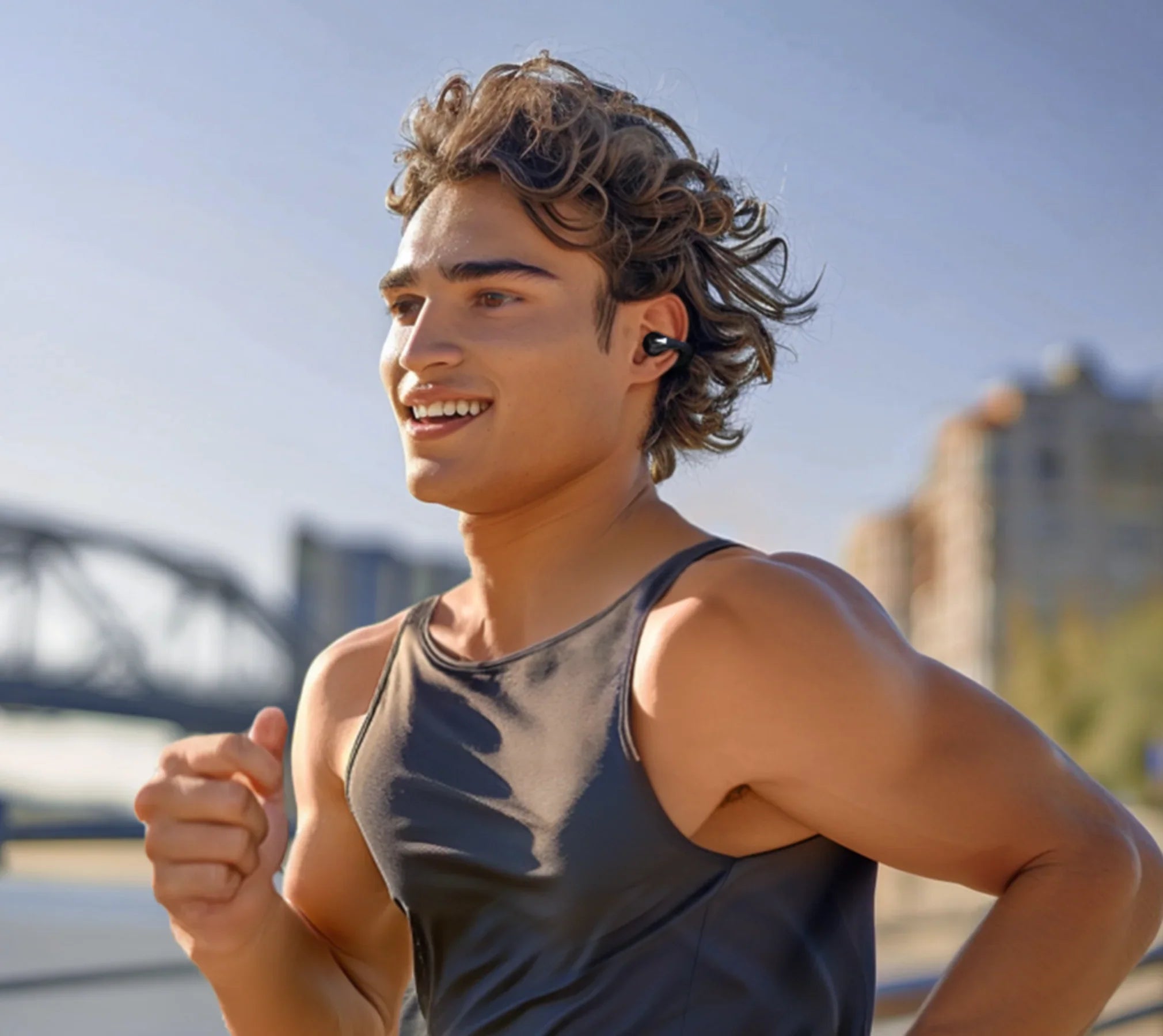 Jeune homme souriant en train de courir avec des écouteurs sans fil, tenue de sport en plein air
