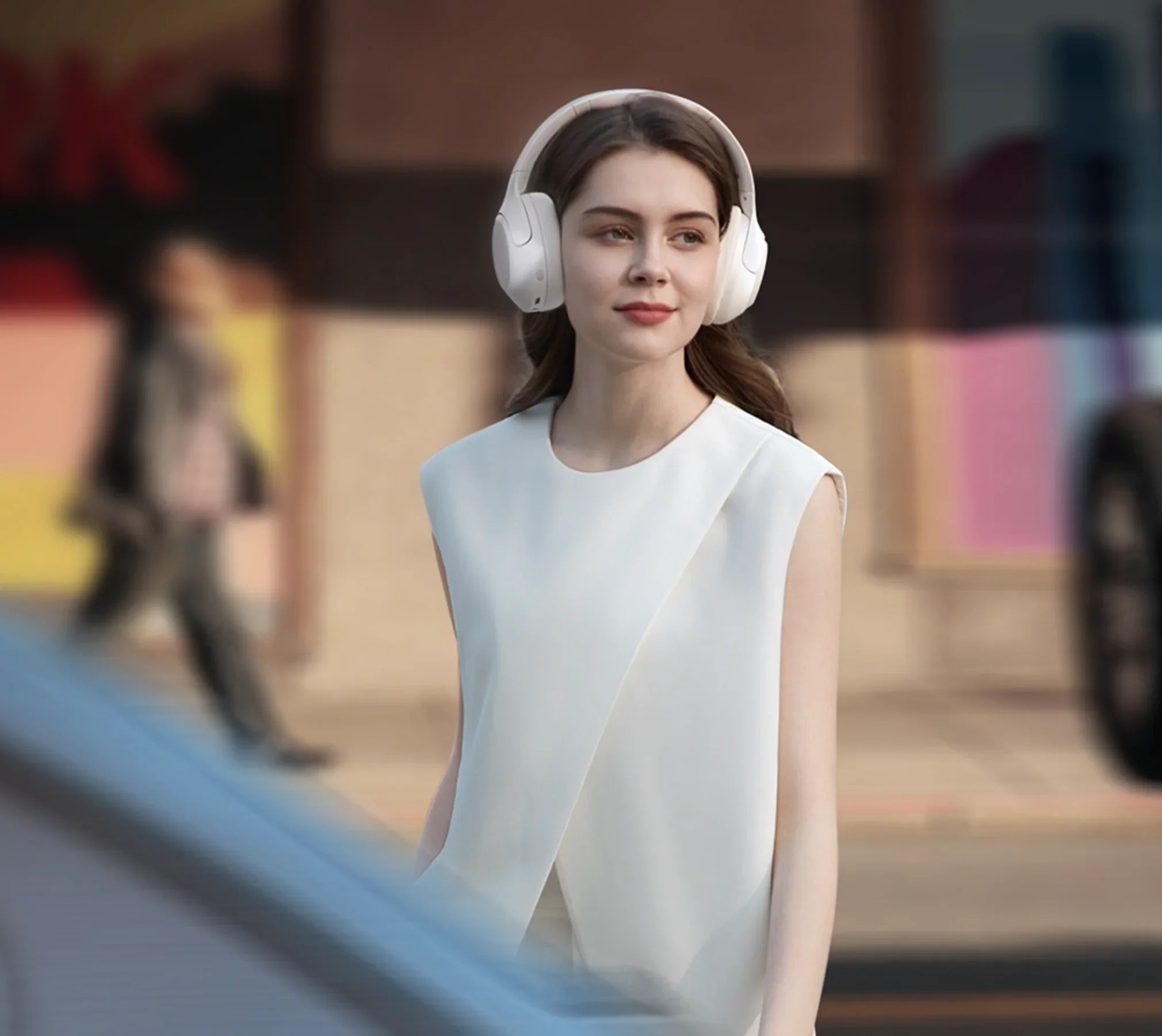 Femme avec des écouteurs blancs Over-Ear dans un environnement urbain, mode élégante, technologie moderne