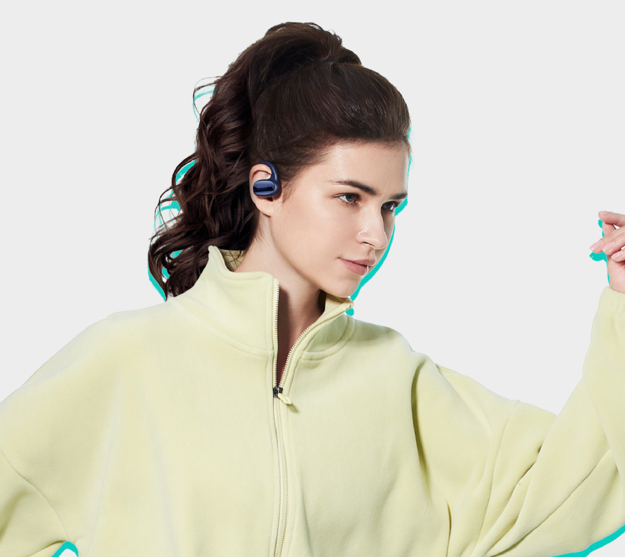 Femme aux cheveux foncés en chignon portant des écouteurs de sport bleus et une veste d'entraînement jaune clair.