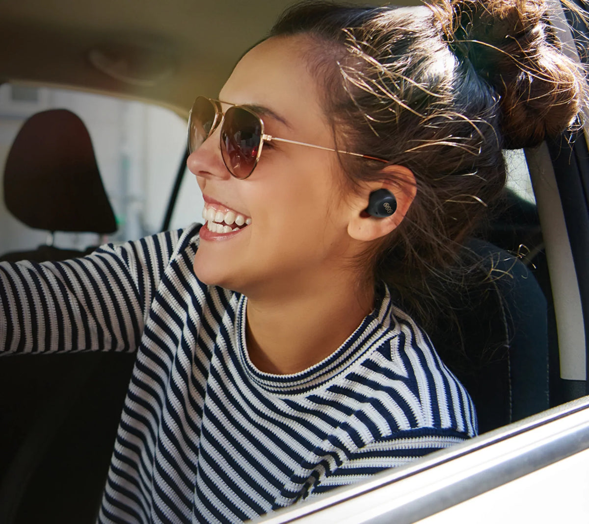 Femme portant des lunettes de soleil et des écouteurs sans fil dans une voiture