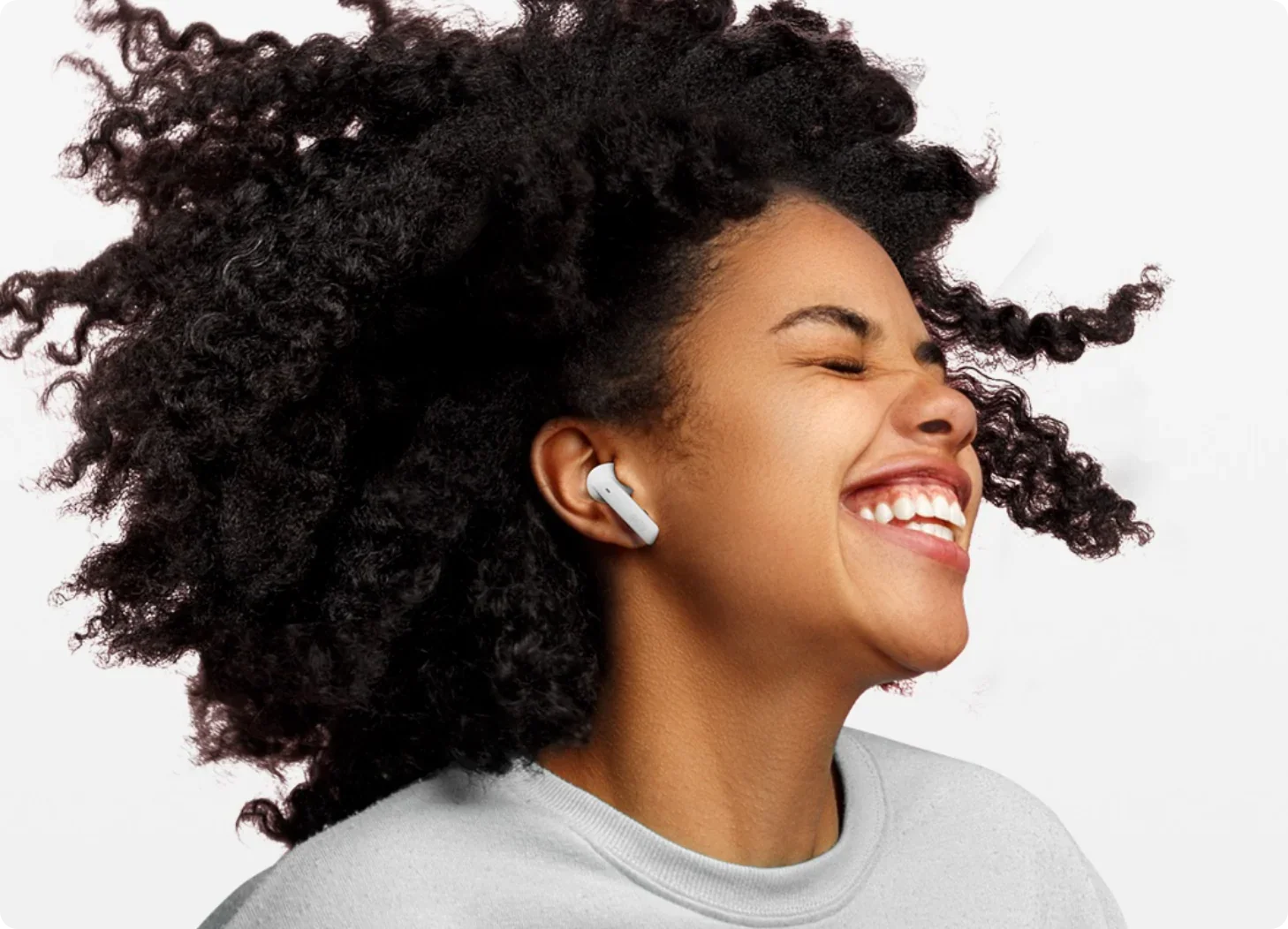 Femme heureuse aux cheveux bouclés portant des écouteurs intra-auriculaires blancs.