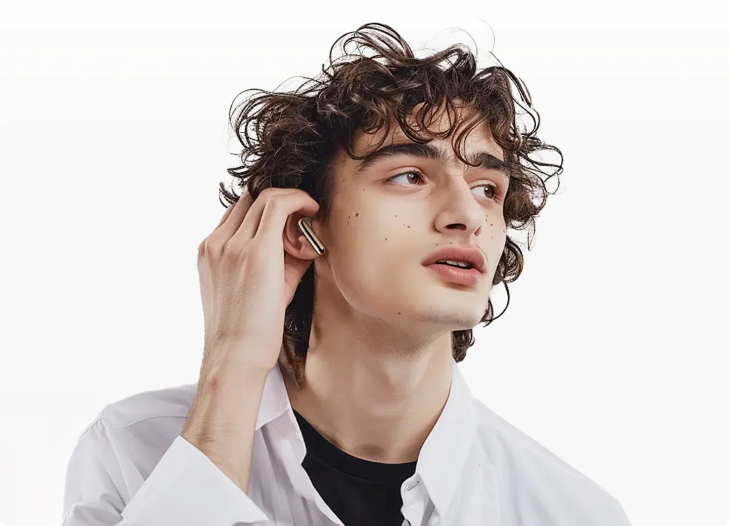 Jeune homme aux cheveux bouclés insérant des écouteurs sans fil dorés, chemise blanche, style de vie moderne.