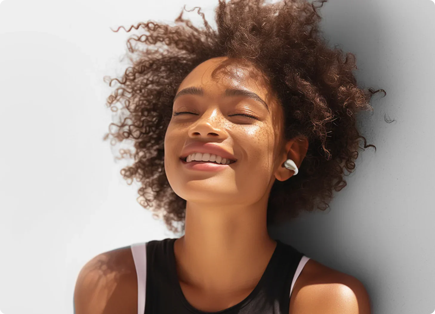 Femme heureuse aux cheveux bouclés portant des écouteurs blancs, appréciant la musique.