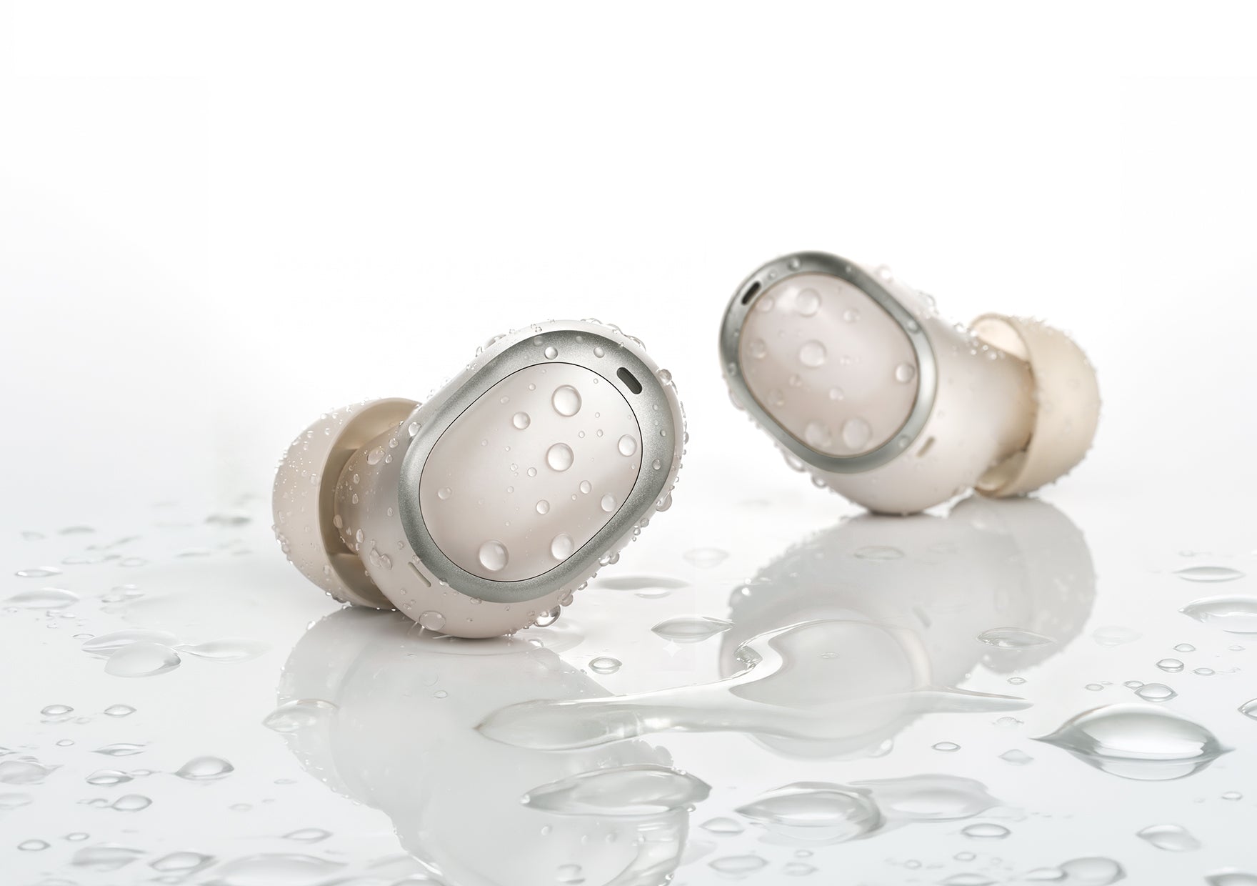 Écouteurs intra-auriculaires blancs étanches avec des gouttes d'eau sur une surface réfléchissante.