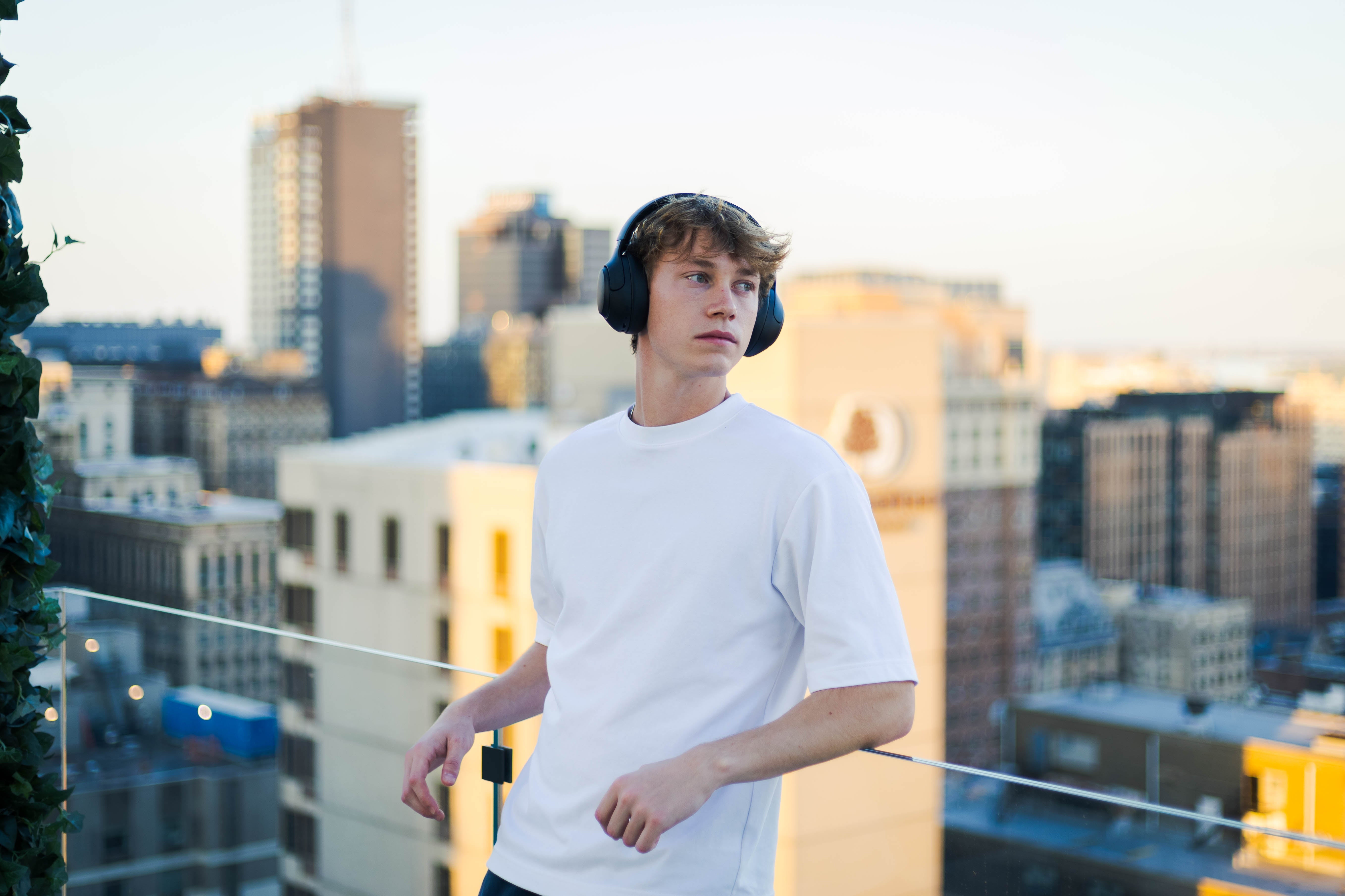Jeune homme avec des écouteurs sur une terrasse sur le toit avec vue sur la ville